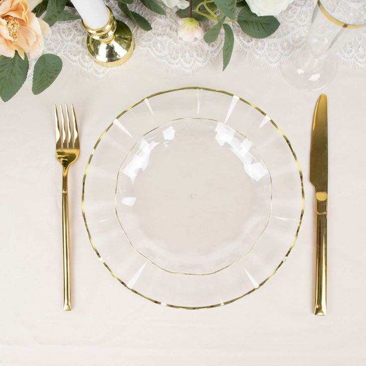 a table setting with white and gold plates, silverware and flowers on the table