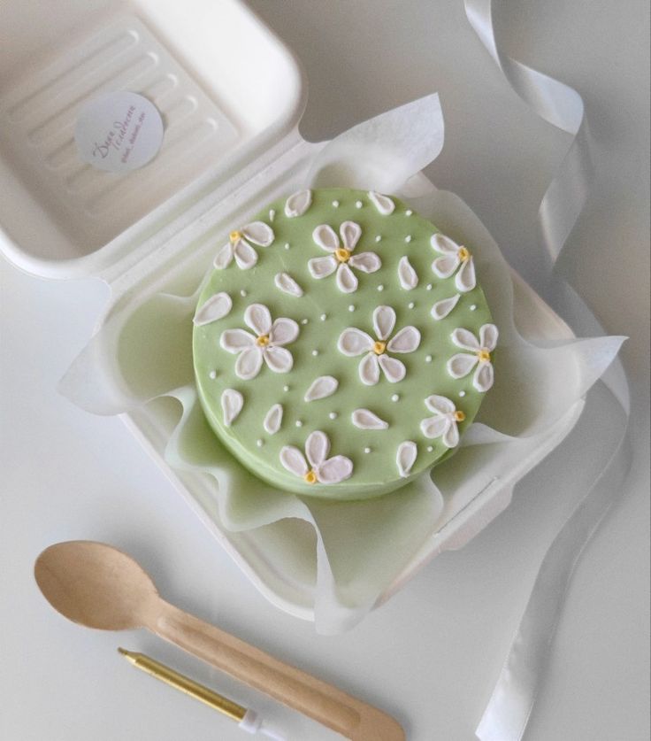 there is a green cake with white flowers on it and two spoons next to it