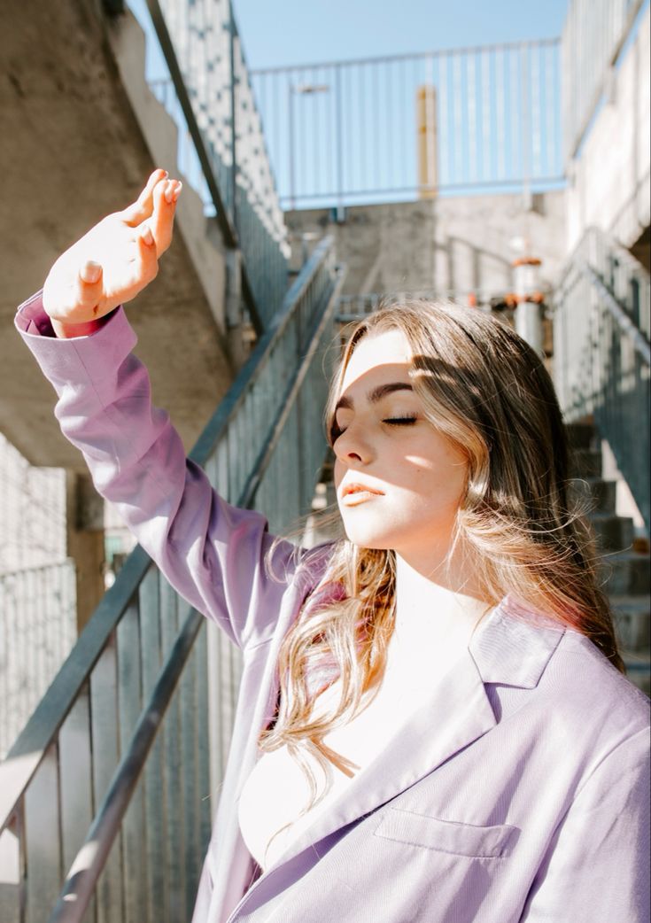 a woman in a purple jacket is holding her hand up to the sky while standing next to some stairs