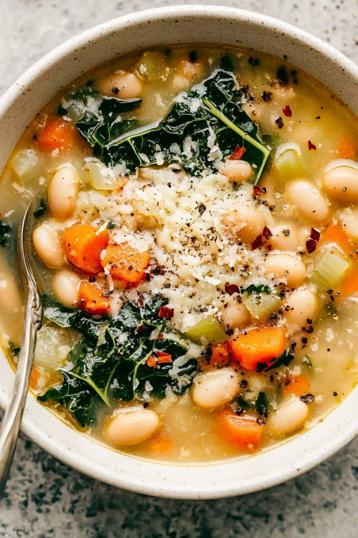 a white bowl filled with beans and spinach on top of a table next to a spoon