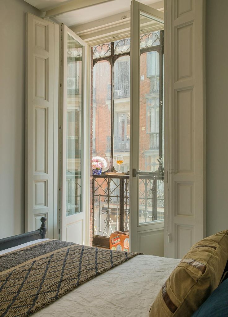 a bed sitting in front of a window next to a white wall and wooden door