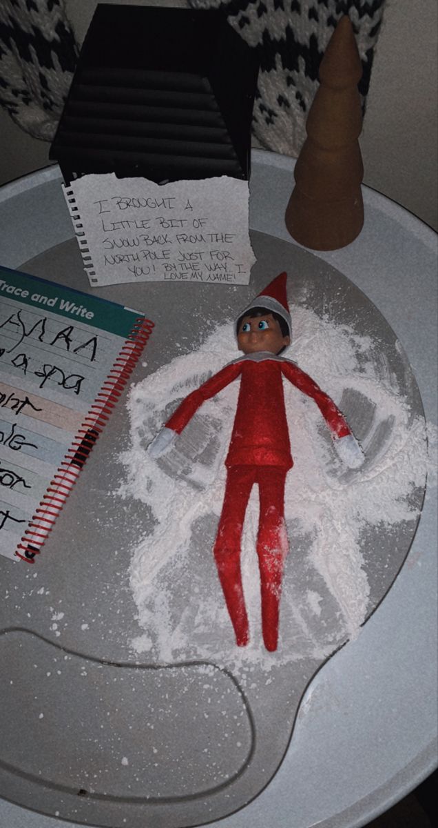 an elf is on top of a cake with writing on it and some papers next to it