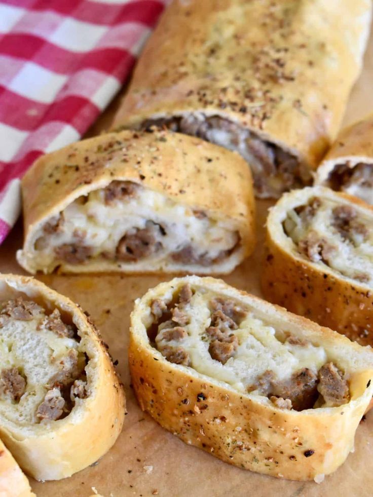 sausage and cheese roll on a cutting board next to a checkered napkin with a red and white towel