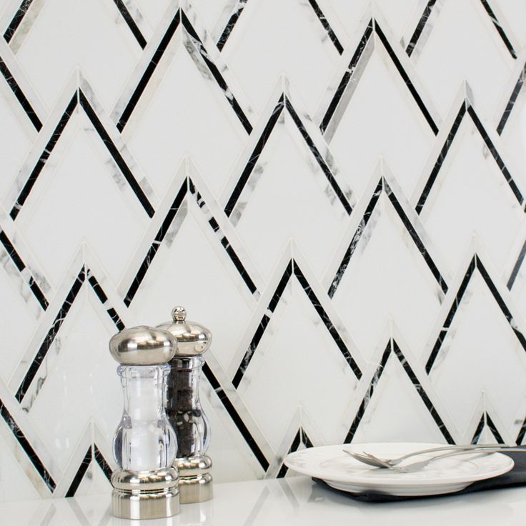 a black and white tiled wall next to a sink with a faucet on it