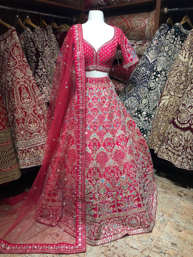 Cerise Red elaborated with sky blue hued floral thread embroidery with pearl, gotta patti, sequence, zari and cut dana work lehenga. Completed look with sequins and zari work blouse and net embroidered blouse. Embrace the whims of rich heritage by adorning this Cerise Red lehenga. Fabric: Raw Silk Size: 38/M Occasion: Wedding Ceremony or Reception WASH CARE INSTRUCTIONS - Please Dry clean only when it is applicable. Slight color variation is possible due to digital photography. Ready to Ship! Red Embellished Sharara For Navratri, Red Mirror Work Sharara For Reception, Red Sharara With Mirror Work For Reception, Red Embellished Dress For Navratri, Red Dola Silk Sharara With Mirror Work, Red Lehenga With Mirror Work And Traditional Drape, Red Embellished Anarkali Sets, Red Lehenga With Mirror Work For Diwali, Red Chinon Dress With Mirror Work