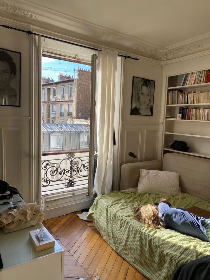 a person laying on top of a green bed in a bedroom next to a window