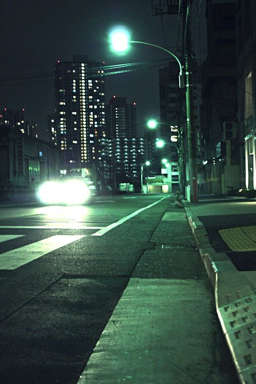 a city street at night with cars driving on the road and buildings in the background