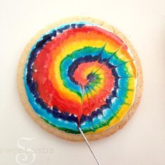 a cookie decorated like a rainbow swirl with a needle in the middle