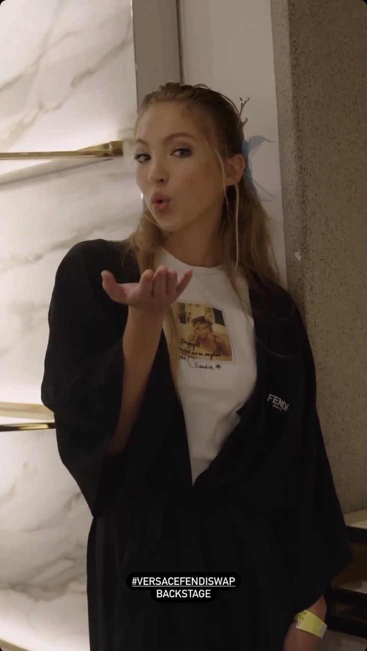 a woman standing in front of a marble wall with her hand up to the side