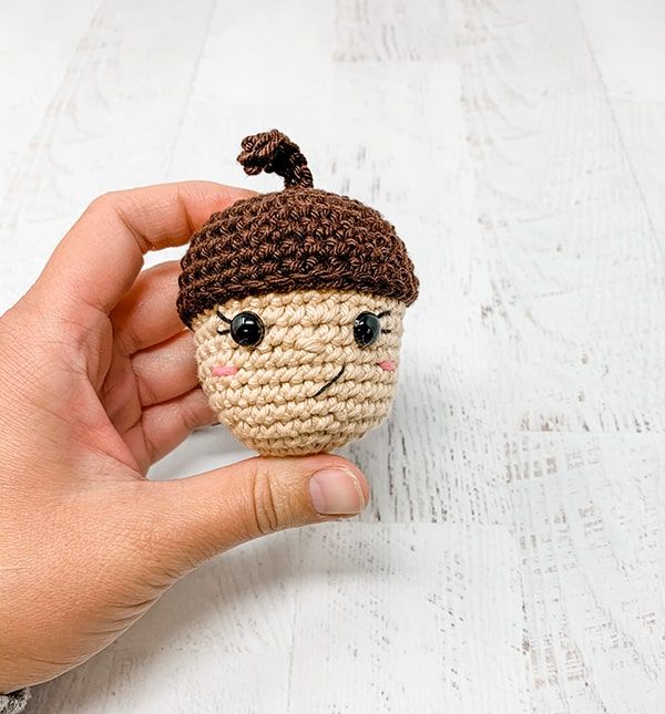 a hand holding a small crocheted doll with a hat on it's head