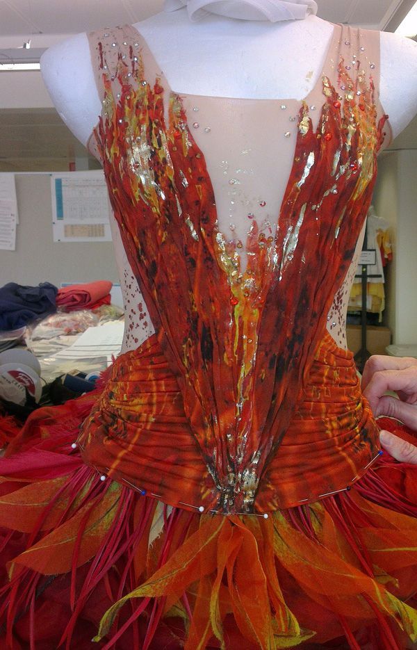 a mannequin with red and orange feathers on it's body, being worked on