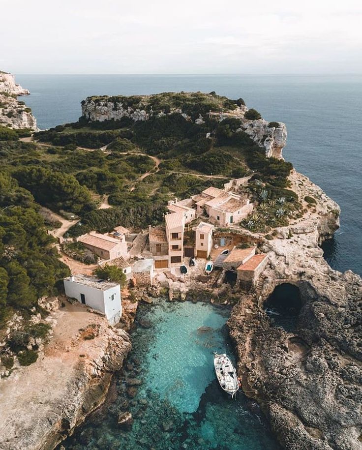 an aerial view of a boat in the water next to a small village on top of a cliff