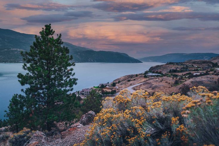 a scenic view of the ocean and mountains at sunset with clouds in the sky above