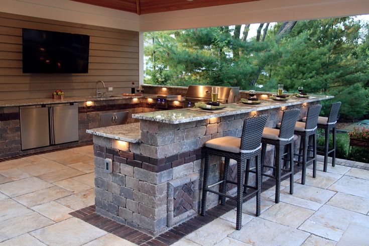 an outdoor kitchen with stone counter tops and bar stools next to the grill area