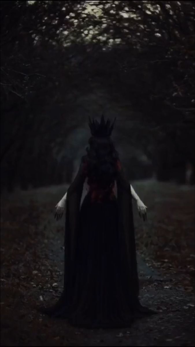 a woman in a black dress and crown standing in the woods with her hands on her hips