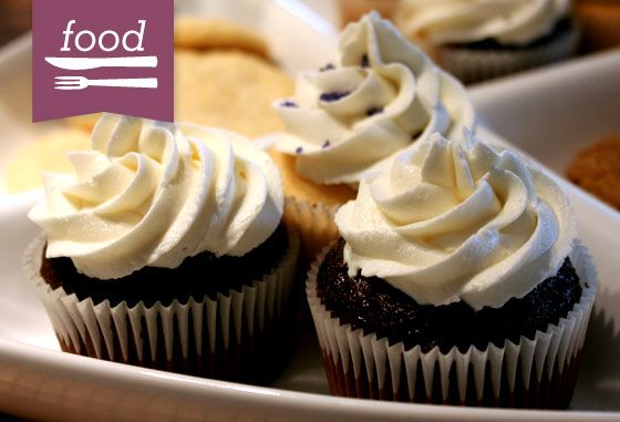 three cupcakes with white frosting on a plate next to other dessert items