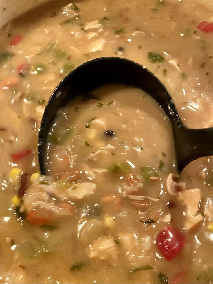 a ladle full of soup is being stirred by a black spoon in the bowl