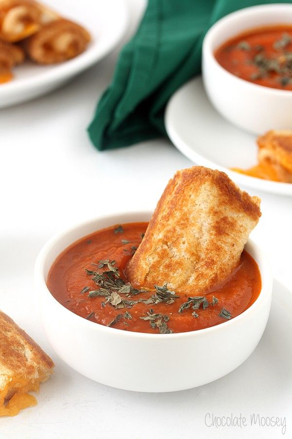 two white bowls filled with tomato soup and grilled cheese on toasted bread sticks