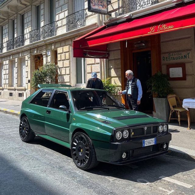 a green car parked in front of a building with two men standing next to it