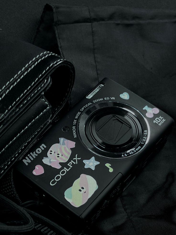 a camera sitting on top of a black bag next to a purse with stickers