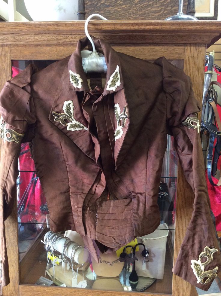 "This brown silk blouse has beautiful leaf appliques of gold metallic soutache on lapels, shoulders, cuffs and the peaks of the standup collar.  The shoulders have ruffles built in and the sleeves are sculpted at the elbows. There is a lovely surprise of three pointed petals making a bit of a peplum  at the small of the back.    A series of hooks and eyes close up the front.  Lined, no boning. In good condition. Shoulder to shoulder 14\" Bust 30\" Waist 22\" Sleeves 15\" under arm; 21\" along the top Length 16\" in front, 19\" at the longest point of the back" Luxury Brown Collared Blouse, Vintage Fitted Brown Blouse, Brown Silk Blouse, Brown V-neck Blouse With Button Closure, Vintage Brown Ruffled Tops, Brown Button-up Blouse With Button Closure, Victorian Blouse, Modern Shoes, Full Skirts