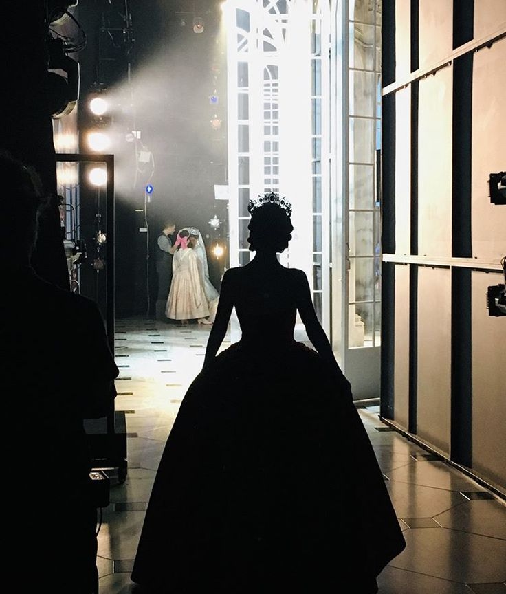 the silhouette of a woman in a black dress is walking into a room with lights