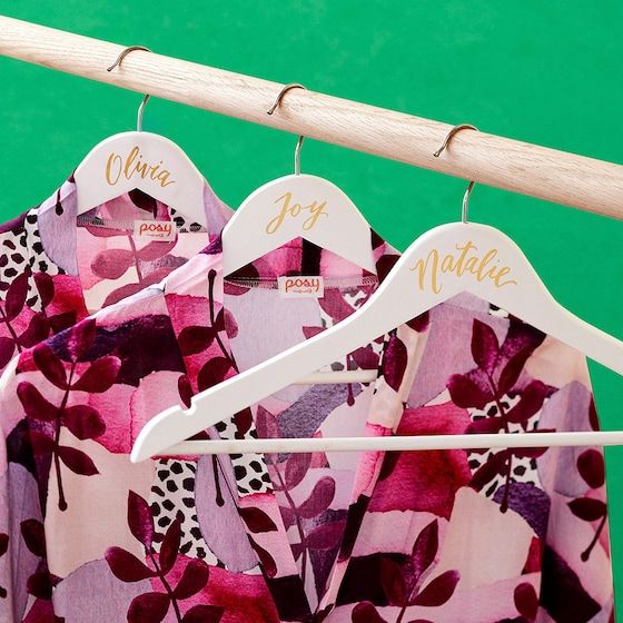 three personalized shirts hanging on a clothes rack with wooden hangers in front of green background