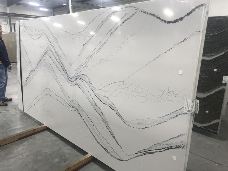 a man standing next to a large white marble slab in a warehouse with two men looking at it