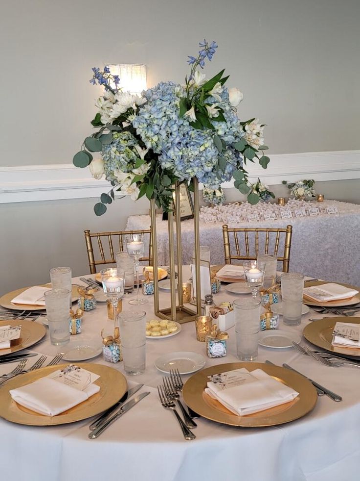 the table is set with silver and gold place settings, napkins, and flowers