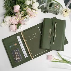 two green notebooks sitting on top of a table next to flowers and a camera