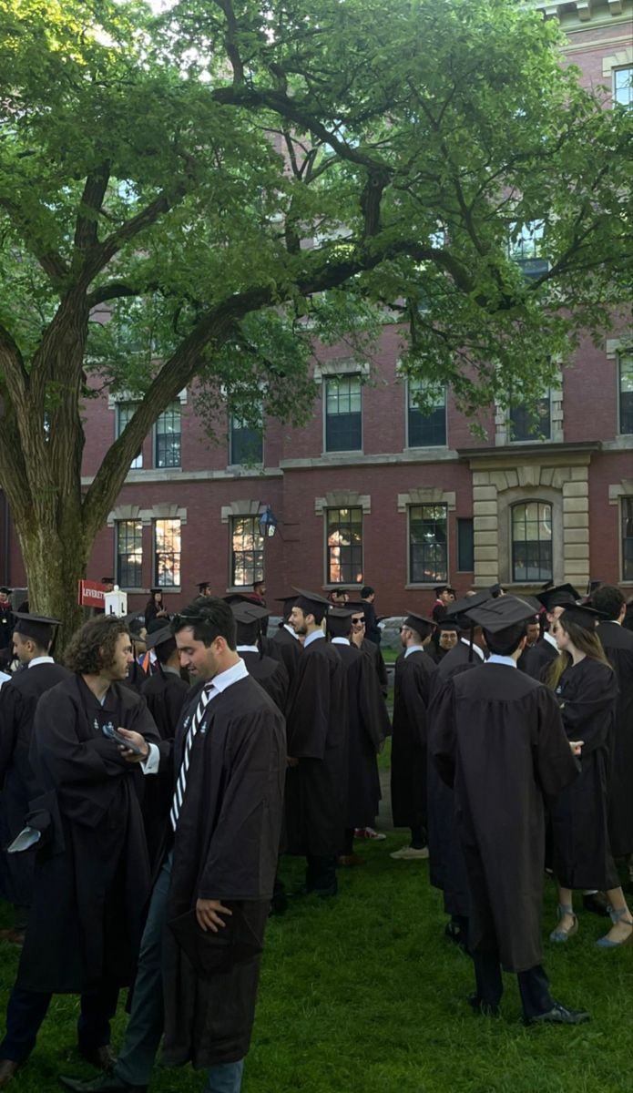 a group of people in graduation caps and gowns standing on the grass near a tree