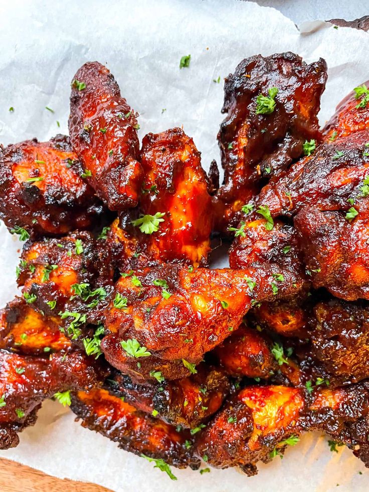 chicken wings covered in barbecue sauce and garnished with parsley on parchment paper