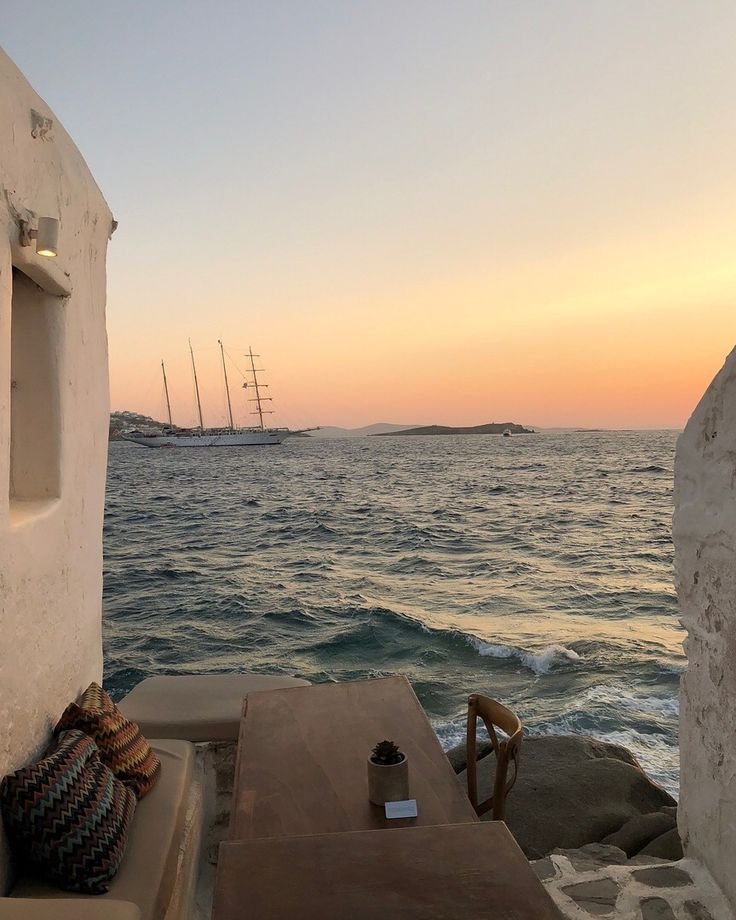 the sun is setting over the ocean and boats are in the water near some rocks