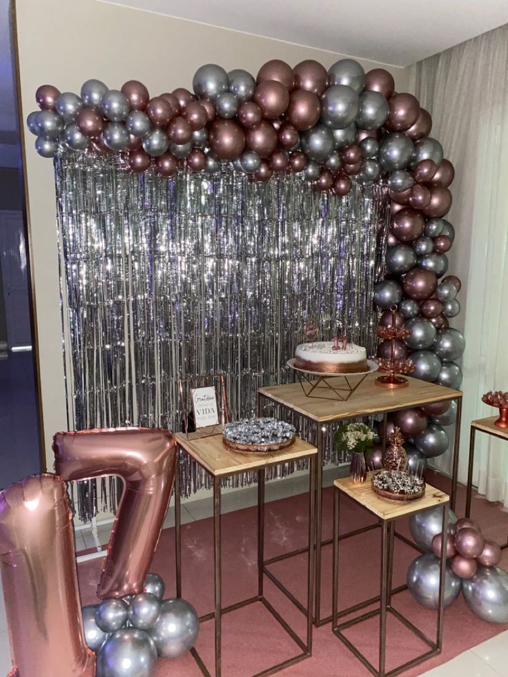 a table topped with lots of balloons next to a wall covered in foil streamers