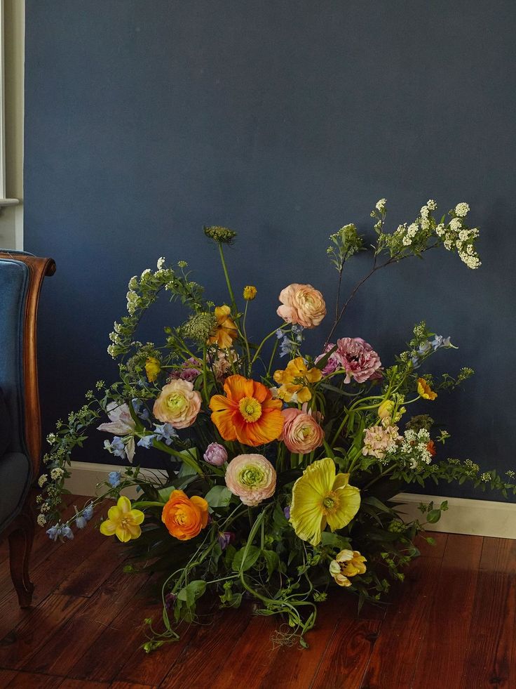 a vase filled with lots of flowers on top of a wooden floor next to a blue wall