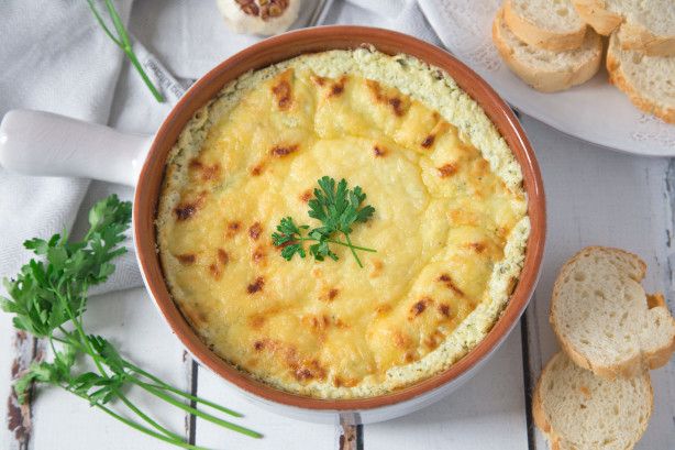 a bowl filled with cheese and bread on top of a white table next to slices of bread