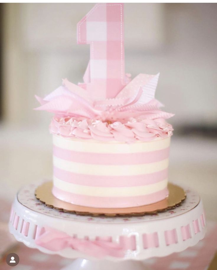 a pink and white striped cake with a number one on it's top tier