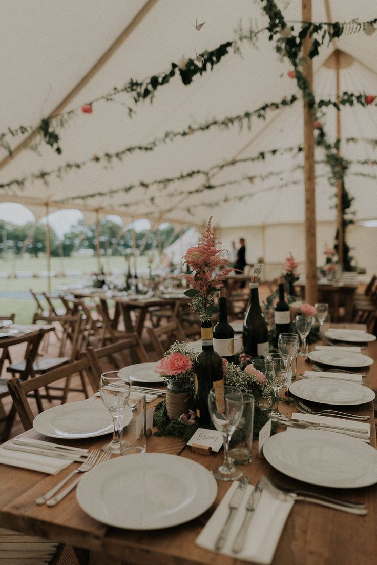 the table is set with white plates and silverware for an elegant wedding reception in a marquee