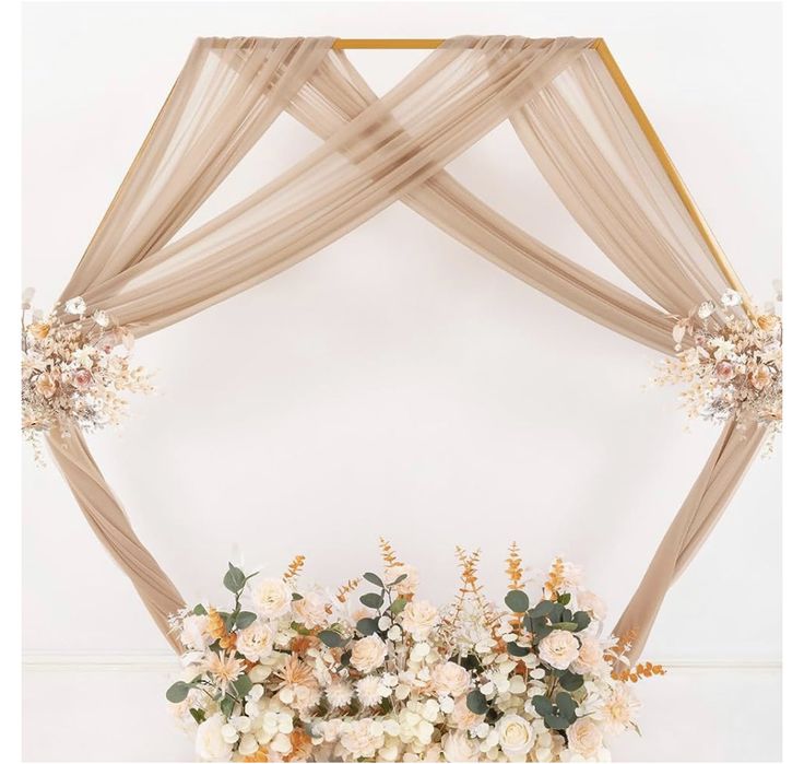 an arrangement of flowers and greenery on a white table clothed arch with sheer drapes