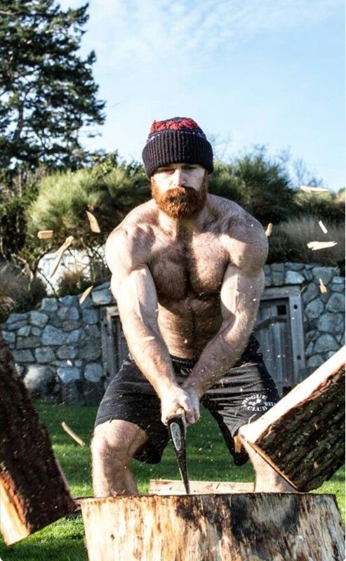 a shirtless man holding an ax in his hands while standing next to a tree