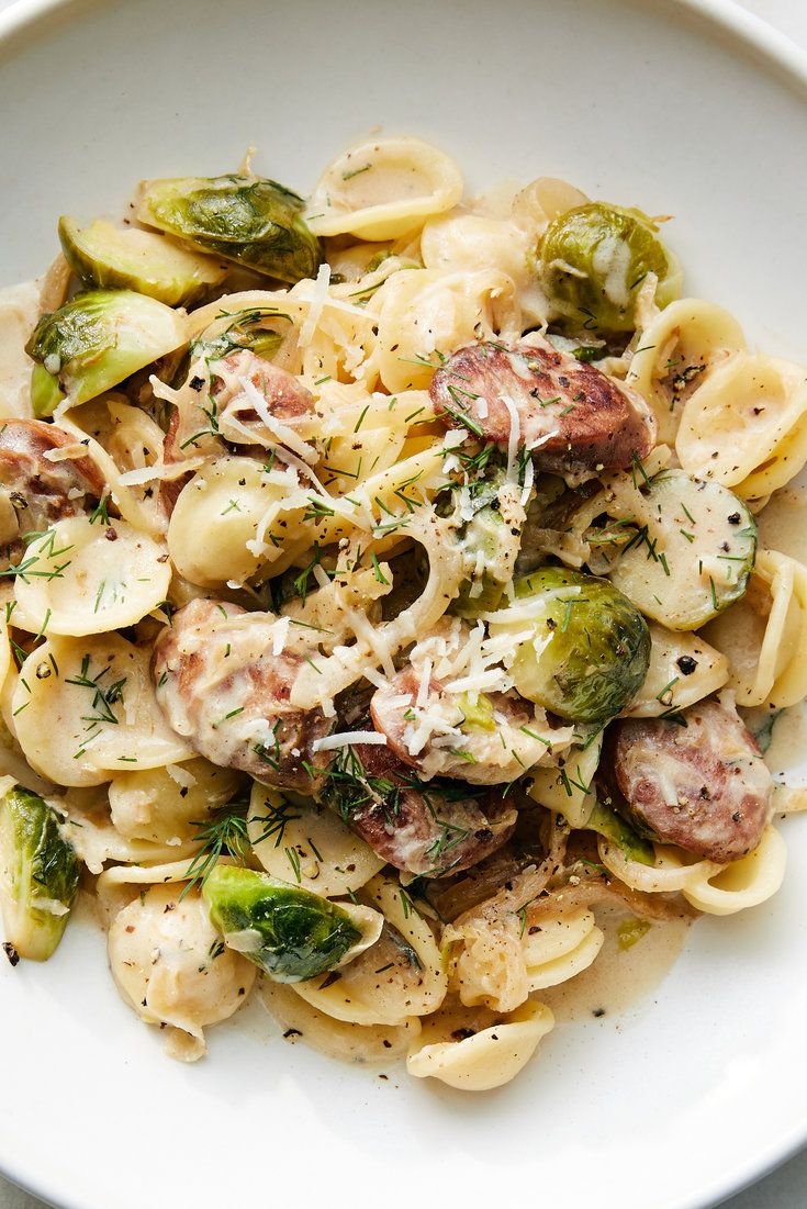 pasta with sausage, broccoli and sprouts in a white bowl on a table