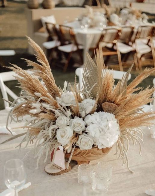 an arrangement of white flowers and wheat stalks in a basket on top of a table