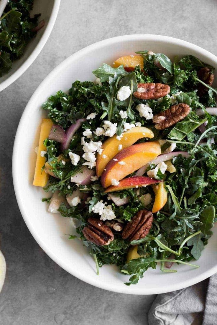 a salad with peaches, pecans and feta cheese in a white bowl