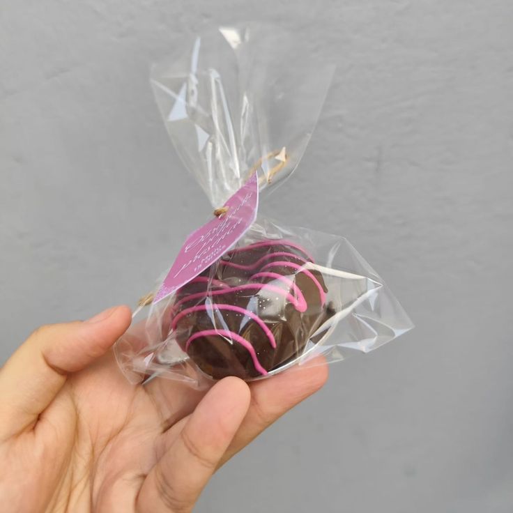 a hand holding a chocolate covered in pink and white sprinkles with a butterfly on top