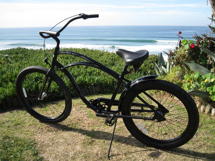 a black bicycle parked on top of a grass covered field next to the ocean and bushes