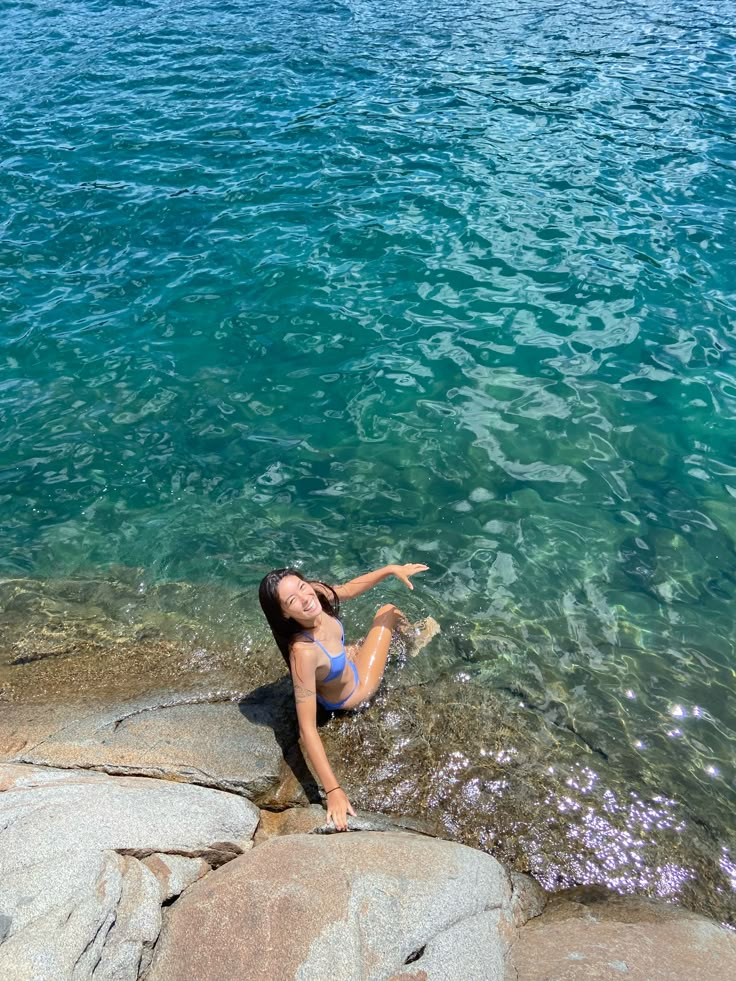 a woman is sitting on some rocks near the water and pointing at something in the distance