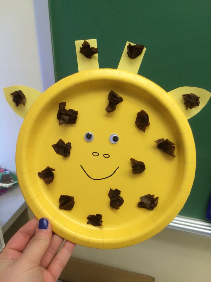 a child's hand holding up a yellow plate with chocolate pieces on it and a smiling giraffe face