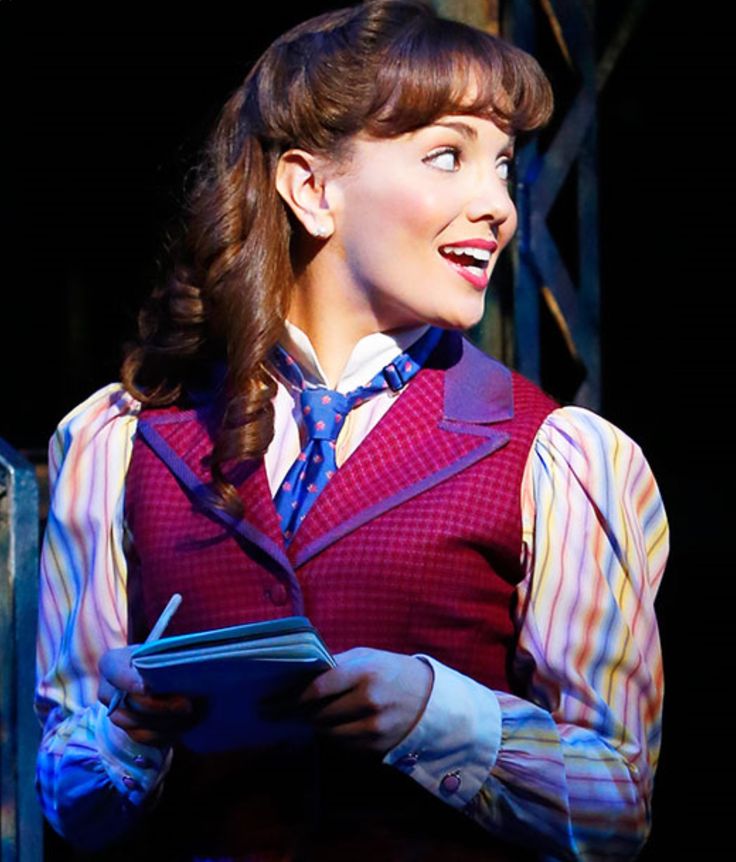 a woman wearing a vest and tie holding a book in her hands while standing on stage