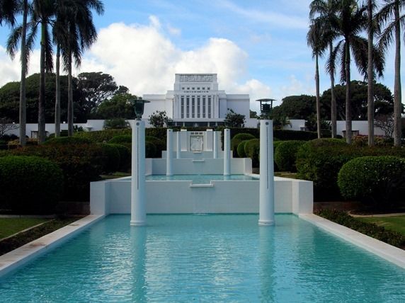 a large pool surrounded by palm trees in front of a white building with columns and pillars