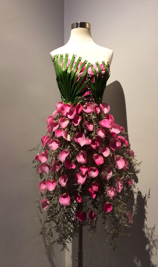 a mannequin with pink flowers and green leaves on it's back, in front of a gray wall